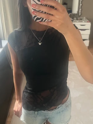 Svart topp med spetsdetaljer - Snygg svart topp med transparenta spetsdetaljer över axlar och midja. Toppen är tight och har korta ärmar samt en rund halsringning. Perfekt för dig som vill ha en trendig och lite edgy look.