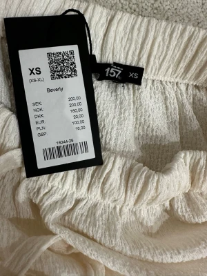 Vit långkjol med volanger från 157 - Säljer en superfin beige långkjol från 157 i storlek XS. Kjolen har volangdetaljer och resår i midjan för en bekväm passform. Materialet är lätt och luftigt, perfekt för varma dagar. Enkel att matcha med olika toppar för en chill look.