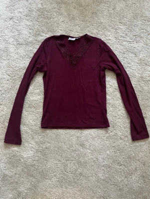 Vinröd långärmad topp Gina Tricot - Vinröd långärmad topp från Gina Tricot med v-ringning och spetsdetaljer runt halsen. Tunn och mjuk i materialet. Enkel men ändå elegant design som passar till mycket.