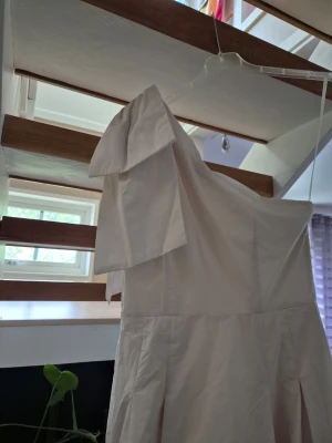 Ljus oneshoulder långklänning - Säljer en elegant ljus långklänning med oneshoulder-design och volangdetalj på axeln. Klänningen har en mjuk, flytande passform och är sydd i ett slätt tyg som ger ett stilrent intryck. Perfekt för dig som vill sticka ut med en unik axelmodell.