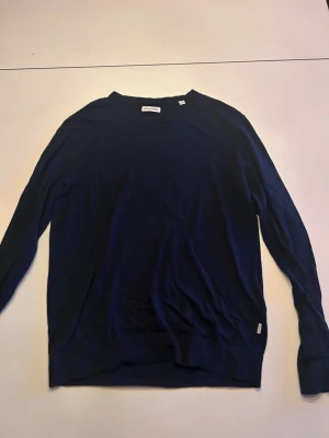 Mörkblå stickad tröja Jack & Jones - Snygg mörkblå stickad tröja från Jack & Jones. Tröjan har rund halsringning och långa ärmar. Tillverkad i ett mjukt och tunt material som passar perfekt till lager-på-lager. Enkel och stilren design utan mönster.