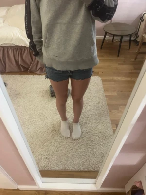 Blå jeansshorts med rå kant - Säljer ett par klassiska blå jeansshorts med rå, fransad kant och femficksmodell. Shortsen har låg midja och är tillverkade i slitstark bomull. Perfekta för varma sommardagar och ger en avslappnad look. Detta är storlek 146 i barn storlek på Gina trickot 