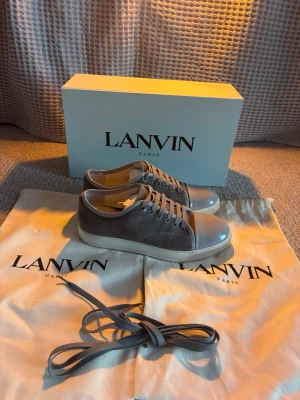 Grå sneakers från Lanvin med lackad tå - Snygga grå sneakers från Lanvin. Kommer med extra skosnören och dustbags. Passar väldigt bra till sommaren. De är väldigt stora i storleken så sitter som en 41 men är uk 5 sulan är 26,5 cm. OBS bara byte mot Maison margiela!