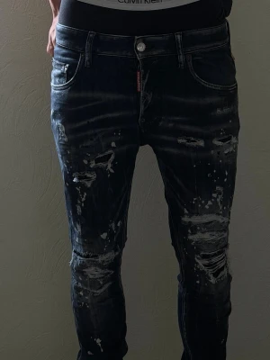 Mörkblå skinny jeans Dsquared2 - Säljer ett par mörkblå skinny jeans från Dsquared2 med slitningar, färgstänk och distressed detaljer. Jeansen har fem fickor, låg midja och en cool, trendig look. Perfekta för dig som gillar streetstyle och vill sticka ut med din outfit.