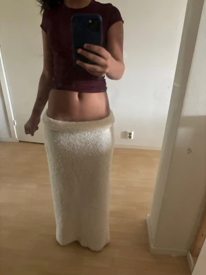 Vit långkjol i fluffigt material - Mysig vit långkjol i fluffigt, stickat material. Kjolen har en rak passform och bred linning som kan vikas ner för en avslappnad look. Perfekt för dig som gillar en enkel men ändå trendig stil. Passar mig som har xs fast den är m. Stretchigt matrial.
