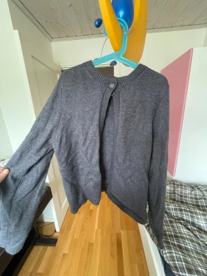 Mörkgrå kofta från Gina Tricot - Mysig mörkgrå kofta från Gina Tricot med rund halsringning och knapp framtill. Koftan har långa ärmar och ribbade muddar vid hals, ärmslut och nederkant. Perfekt att slänga över en t-shirt för en chill look.storlek S