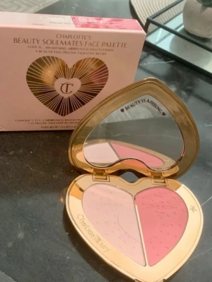 Charlotte Tilbury Beauty Soulmates Rougepalett - Snygg hjärtformad rougepalett från Charlotte Tilbury med två nyanser: en ljusrosa highlighter (Airbrush) och en varm rosa rouge (Love Blush). Lyxigt guldig förpackning med spegel och detaljerad design. Perfekt för att skapa en fräsch glow och markerade kinder.
