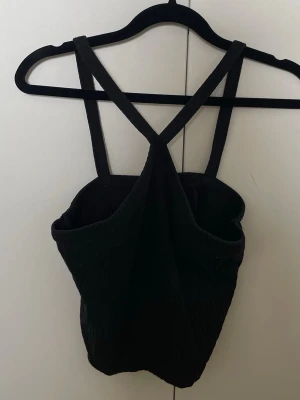 Svart ribbad linnetopp Gina Tricot - Snygg svart ribbad cropped linnetopp med halterneck från Gina Tricot med smala axelband som korsas i ryggen. Toppen är figurnära och har en enkel, stilren design som passar perfekt till jeans eller kjol. Perfekt för dig som gillar minimalistisk stil.