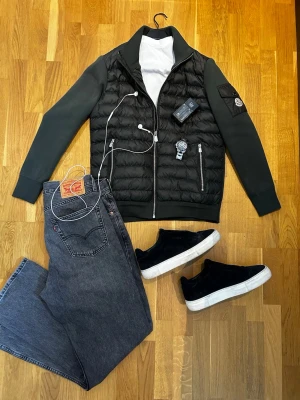  Cardigan från Moncler - Snygg svart hybridjacka från Moncler med quiltad front och släta ärmar. Jackan har dragkedja framtill, två fickor med dragkedja och en patch med Moncler-logga på ärmen. Materialmix med vadderad kropp och mjuka ärmar ger en modern look.