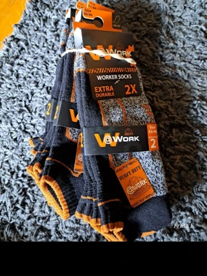 Svarta och grå arbetssockor 6 par - Tjocka och slitstarka arbetssockor från @Work i svart och grått med orange detaljer. Perfekta för dig som behöver extra hållbara strumpor. Säljs i 2-pack och har en sportig look med ribbade partier och markerade sömmar.