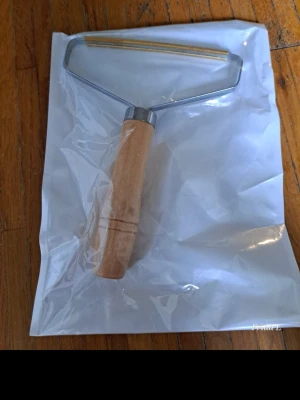 Luddroller med trähandtag - En luddroller med ergonomiskt handtag i ljust trä och metallram. Perfekt för att ta bort ludd, hår och damm från kläder, soffor eller andra textilier. Rullen har en bred metallram och är enkel att använda för snabb rengöring.