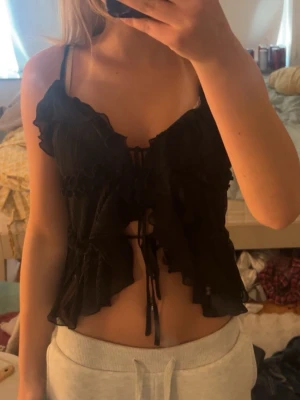 Svart linnetopp med snörning från New Yorker - Säljer en svart linnetopp från Amisu med tunna axelband, volangdetaljer och snörning framtill. Toppen är croppad och har en feminin, luftig look som passar perfekt till sommaren. Materialet känns lätt och svalt. Aldrig andvänd.
