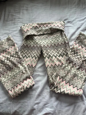 Mönstrade leggings med zigzag-mönster - Säljer ett par leggings med snyggt zigzag-mönster i vitt, svart, rosa och beige. De har hög midja och stretchigt material som sitter skönt. Perfekta för dig som vill sticka ut med ett coolt mönster och bekväm passform.