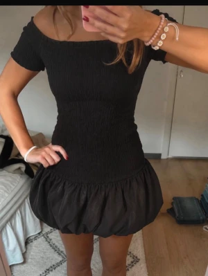 Svart kort offshoulder klänning - !!den är i stl L men jag brukar ha stl xs-s, så skulle säga att den passar vem som!! Trendig svart kort klänning med offshoulder-design och puffig ballongkjol. Överdelen är smockad och sitter tight mot kroppen medan kjolen har volym. Perfekt för dig som vill ha en unik och snygg look. 