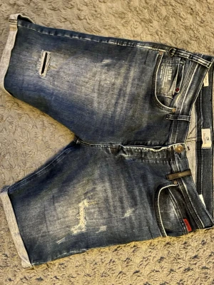 Blå jeansshorts från LTB - Säljer ett par blå jeansshorts från LTB med slitna detaljer och uppvikta benslut. Klassisk femficksmodell med knappgylf och coola slitningar framtill. Perfekta för en avslappnad och trendig stil.
