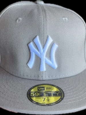 Grå New Era Yankees 59Fifty keps - Storlek 58,6 cm (7 1/8)Snygg grå 59Fifty keps från New Era med broderad vit New York Yankees-logga framtill och MLB-logga bak. Klassisk flat brim och strukturerad passform. Tillverkad i slitstark bomullsmix, perfekt för dig som gillar streetwear och sportig stil.