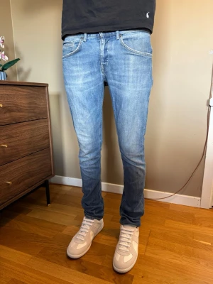 Dondup george jeans - Säljer ett par ljusblå slim fit jeans från dondup med klassisk femficksmodell och snygga slitningar. Jeansen har normal midja, dragkedjegylf och är tillverkade i mjuk denim med lite stretch för extra komfort.