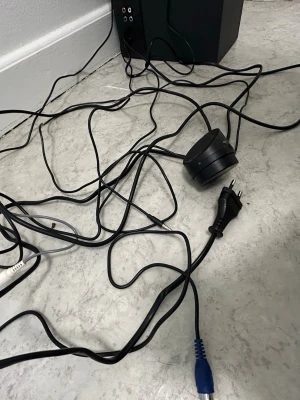 Logitech svart trådlös högtalare - Säljer en svart trådlös högtalare från Logitech med flera anslutningsmöjligheter, inklusive RCA och 3,5 mm. Högtalaren har en robust, fyrkantig design i plast och metall, och medföljande kablar för enkel installation. Perfekt för att boosta ljudet till dator eller TV.