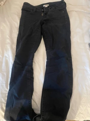 Svarta bootcut jeans från Gina Tricot  - Snygga svarta jeans från Gina med bootcut-modell och klassiska fem fickor. Jeansen har detaljerade bakfickor (något slags broderi) med knapp, däremot har ens knappen lossnat. De är i bra skick, liten defekt längs ner ( se bild 3&4)