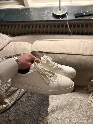 Vita Loubs - Säljer ett par stilrena vita sneakers från Christian Louboutin med klassisk röd sula och signaturdetaljer undertill. Skorna har lågt skaft, vita skosnören och är tillverkade i slätt läder. Perfekta för dig som gillar exklusiv och clean stil. Bra skick - bara smutsiga under. Pris kan diskuteras.