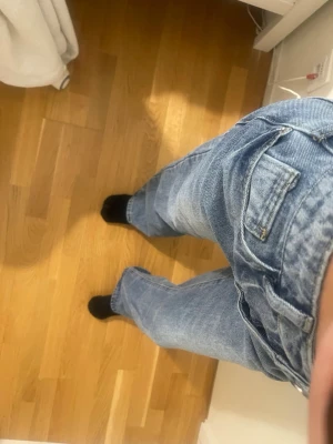 Blå raka jeans med hög midja - Säljer ett par klassiska blå jeans med rak passform och hög midja. Jeansen har fem fickor, bälteshällor och stängs med knapp och dragkedja. Perfekta till en avslappnad stil och passar till det mesta. Materialet är kraftig denim i bomull.
