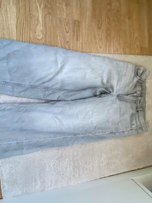 Ljusgråa raka jeans - Säljer ett par ljusgråa jeans med rak passform och klassisk femficksdesign. Jeansen har hög midja och breda ben, perfekta för en avslappnad och trendig look. Materialet är denim i bomull. Inga synliga loggor eller märken.
