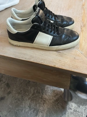 Svarta och vita sneakers från Valentino - Snygga sneakers från Valentino i svart och vitt läder med klassisk låg siluett. Skorna har svarta snören, vit sula och en bred vit panel på sidan. Perfekta för dig som gillar stilrena och exklusiva detaljer.