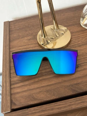 Blå EPA raggar solglasögon  - Säljer ett par riktigt snygga solglasögon med svart båge och spegelblått glas i shield-modell. Nya. Unisex. Skickar gärna i bundle. Glasen har en cool blå-lila ton och ger en futuristisk vibe. Perfekta för dig som vill sticka ut och addera edge till din outfit.