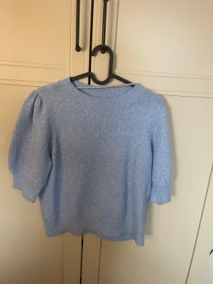 Ljusblå stickad tröja Vero Moda - Ljusblå stickad tröja från Vero Moda med rund halsringning och puffade halvlånga ärmar. Tröjan har ribbstickade detaljer vid halsen och ärmsluten. Perfekt för att skapa en soft och trendig look.