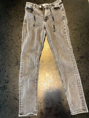 Calvin Klein grå jeans W27 – high rise skinny - Snygga grå jeans från Calvin Klein med snördetalj i midjan. High rise skinny modell med stretch och smickrande passform. Trendig grå tvätt.  Lite slitage i grenen, se sista bild. Därför lägre pris. Storlek: W27 L30 Modell: High rise skinny Färg: grå Skick: bra skick  Perfekta till vardag eller fest.