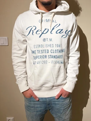 Extremt eftertraktad Vintage replay hoodie - Snygg vit hoodie från Replay med blått tryck framtill och textdetaljer. Klassisk känguruficka, dragsko i huvan och ribbade muddar. Perfekt för en avslappnad streetwear-look. Tillverkad i mjukt bomullsmaterial för extra komfort.