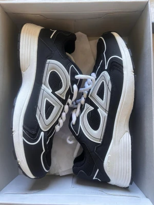 Svarta CD sneakers - Säljer ett par svarta sneakers från CD med vita och grå detaljer. Skorna har en chunky vit sula, vita skosnören och meshpaneler för extra ventilation. Snygg design med kontrasterande linjer och logga på sidan. Perfekta för dig som gillar streetwear och modern stil.