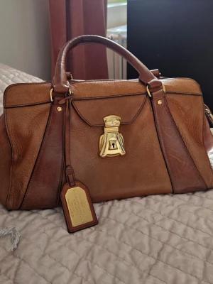 Lauren by Ralph Lauren handbag  - Elegant Lauren by Ralph Lauren Winslow Lock Satchel - Tan 🤎 Elegant och tidlös handväska i äkta läder med klassiskt guldfärgat lås. Väskan har en strukturerad form och lyxig känsla – passar både till vardag och mer uppklädda tillfällen.