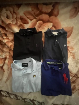 4-pack pikétröjor från Polo Ralph Lauren - Säljer fyra pikétröjor från Polo Ralph Lauren i olika färger: svart, mörkblå, ljusblå och blå med röd logga. Klassisk krage och knappar framtill. Perfekta för en clean och stilren look. Alla tröjor har broderad logga på bröstet.