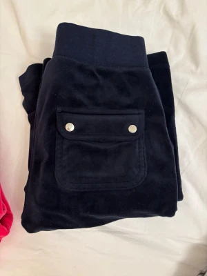 Marinblå mjukisbyxor med ficka - Säljer ett par svarta mjukisbyxor i mjuk velour med bred mudd i midjan och en stor ficka med lock och silverfärgade knappar på sidan. Perfekta för chill dagar och riktigt sköna att ha på sig.            De är i passformen straight 