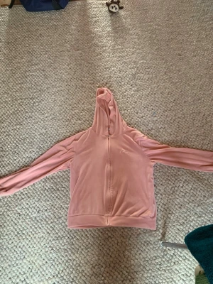 Rosa hoodie med broderad text - Mjuk rosa hoodie med dragkedja framtill och broderad text 'love' på bröstet. Tillverkad i ett lent, fleece-liknande material och har en klassisk huva. Perfekt för en chill och avslappnad stil.