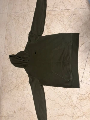  Nike hoodie med huva - Säljer en  hoodie från Nike med klassisk huva och stor magficka framtill. Diskret Nike-logga på bröstet. Hoodien har långa ärmar och är gjord i mjukt bomullsmaterial som känns skönt mot huden. Perfekt för en avslappnad och sportig stil.