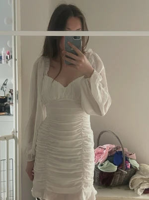 Vit klänning  - Säljer en elegant vit klänning från NLY Trend med långa ärmar och rynkade detaljer. Klänningen har en dragkedja i ryggen och en volangkant nedtill. Perfekt för stunden.