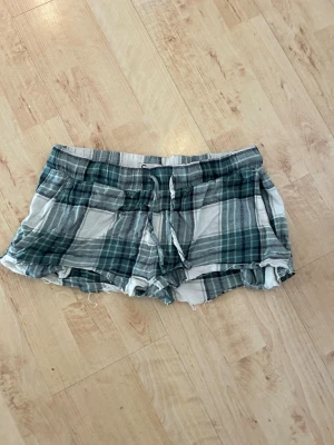Grönrutiga shorts med snörning - Säljer ett par grön- och vitrutiga shorts med snörning i midjan. De har avslappnad passform, råa kanter och mjukt bomullsmaterial. Perfekta för varma dagar och chill stunder. Egengjorda, omsydda.