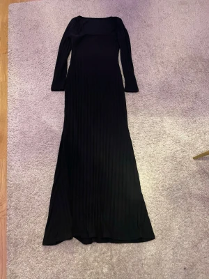 Svart ribbad maxiklänning - Lång svart maxiklänning med ribbad struktur och fyrkantig urringning. Klänningen har långa ärmar och är figurnära i modellen. Perfekt för dig som gillar en stilren och enkel look.