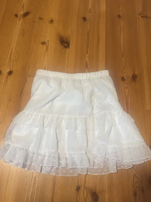 Vit volangkjol från SHEIN - Supersöt vit kortkjol från SHEIN med volanger och prickigt mönster. Kjolen har resår i midjan och är gjord i lätt och luftig polyester, perfekt för varma dagar. Passar till många olika stilar och är enkel att matcha.