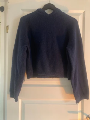 Mörkblå hoodie i mjukt material - Mysig mörkblå hoodie med lång ärm och huva. Tröjan är stickad i ett fluffigt, mjukt material och har ribbade muddar vid ärmslut och nederkant. Perfekt för dig som gillar en avslappnad och bekväm stil.