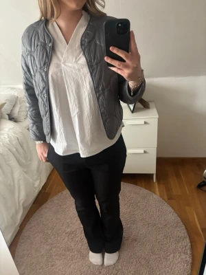 Grå quiltad kort jacka mango - Snygg grå quiltad jacka med rundad halsringning och tryckknappar framtill. Jackan är kort i modellen och har ett diskret mönster i tyget. Perfekt för dig som vill ha en jacka som är lätt att matcha både för vardag och för mer uppklädda tillfällen. Jackan passar både för vår och höst.