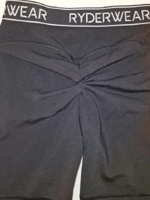 Svarta shorts från Ryderwear - Svarta shorts från Ryderwear med hög midja och elastisk linning med logga. Shortsen har en scrunch-detalj bak som formar rumpan snyggt 🖤 Perfekt till sommaren.
