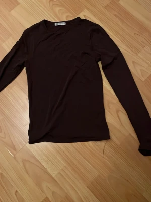 Mörkbrun långärmad topp från Zara - Säljer en enkel och stilren mörkbrun långärmad topp från Zara. Toppen har rund halsringning och är tillverkad i ett mjukt material som känns skönt mot huden. Perfekt att matcha med jeans eller kjol för en clean look.