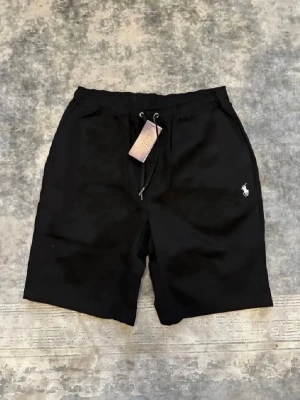 Svarta shorts från Polo Ralph Lauren - Svarta shorts från Polo Ralph Lauren med dragsko i midjan och klassisk logga broderad på vänster ben. Shortsen har fickor fram och en bakficka. Står S men är stora i storleken. Säg längden i vikten på dig kan jag ge dig ett svar