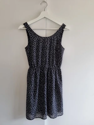 Svart blommig sommarklänning H&M - Söt klänning med små vita blommor och cut out på ryggen. Klänningen har rundad halsringning och resår i midjan för en bekväm passform. Perfekt skick.