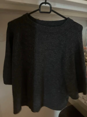 Mörkgrå stickad tröja - En enkel och stilren mörkgrå stickad tröja med rund halsringning och långa ärmar. Tröjan har en mjuk och lite lös passform, perfekt för lager på lager. Materialet ser ut att vara ull eller en ullmix som känns varm och skön
