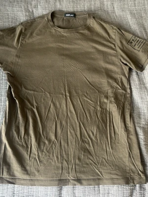 Olivgrön t-shirt från Replay - Snygg olivgrön t-shirt från Replay med tryck på ena ärmen. Klassisk rund halsringning och korta ärmar. Tillverkad i mjuk bomull som känns skön mot huden. Perfekt för en avslappnad och stilren look.