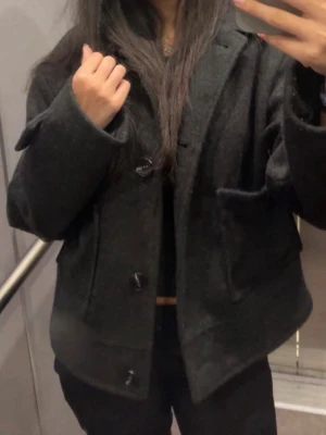 Svart kappa med knappar - Stilren svart kappa i ullmix med stora knappar framtill och två fickor. Kortare modell med klassisk krage och raka ärmar. Perfekt för dig som vill ha en enkel men snygg jacka till hösten eller våren💞